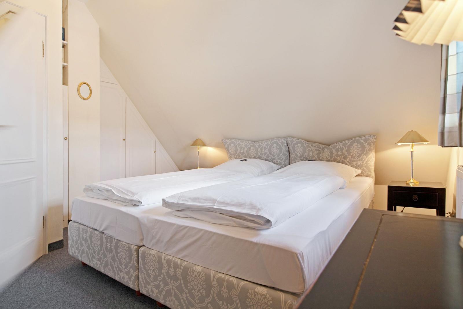 Bedroom with double bed, nightstand, and lamp under sloped ceiling.