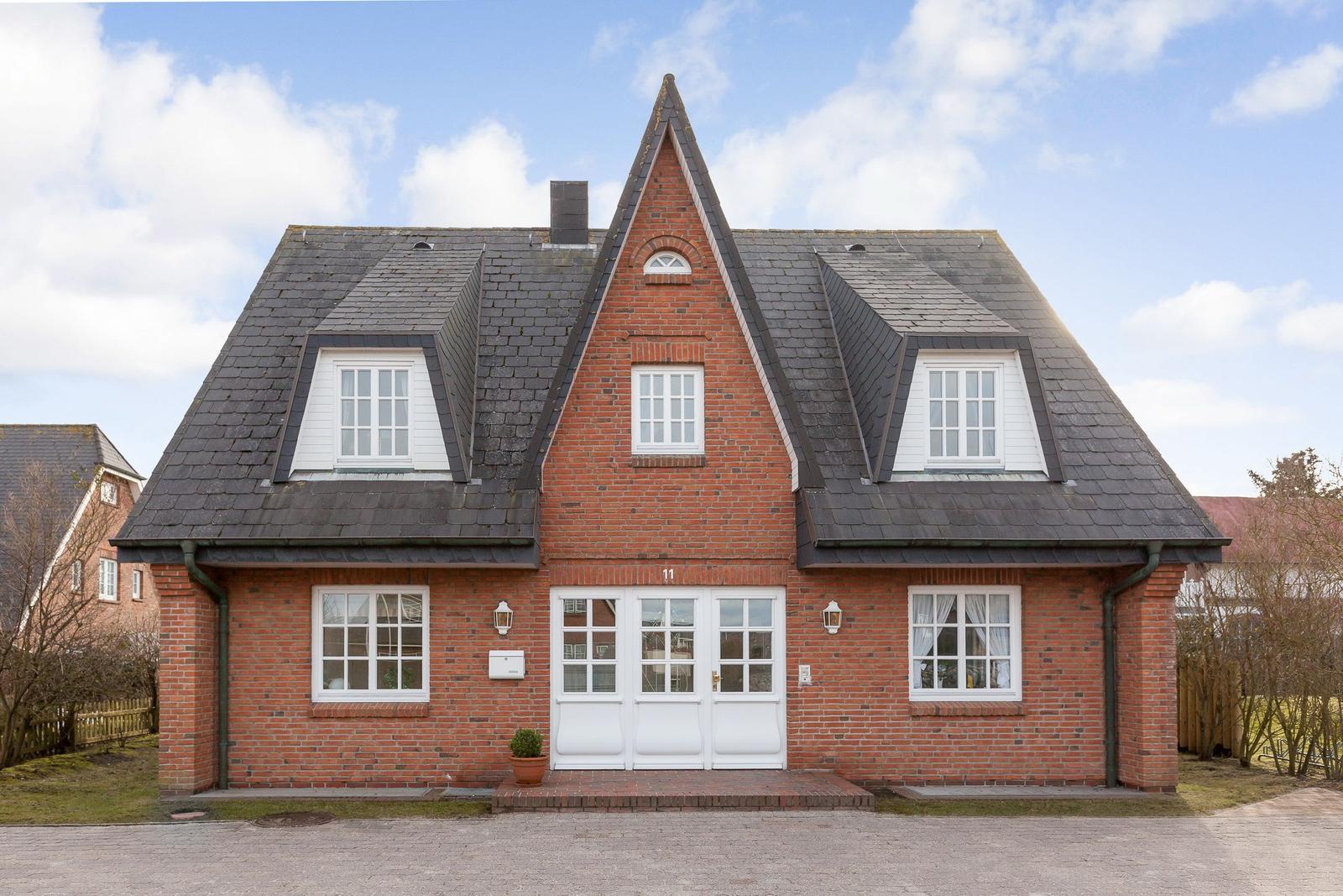 Red brick house with white windows and dormers under blue sky.