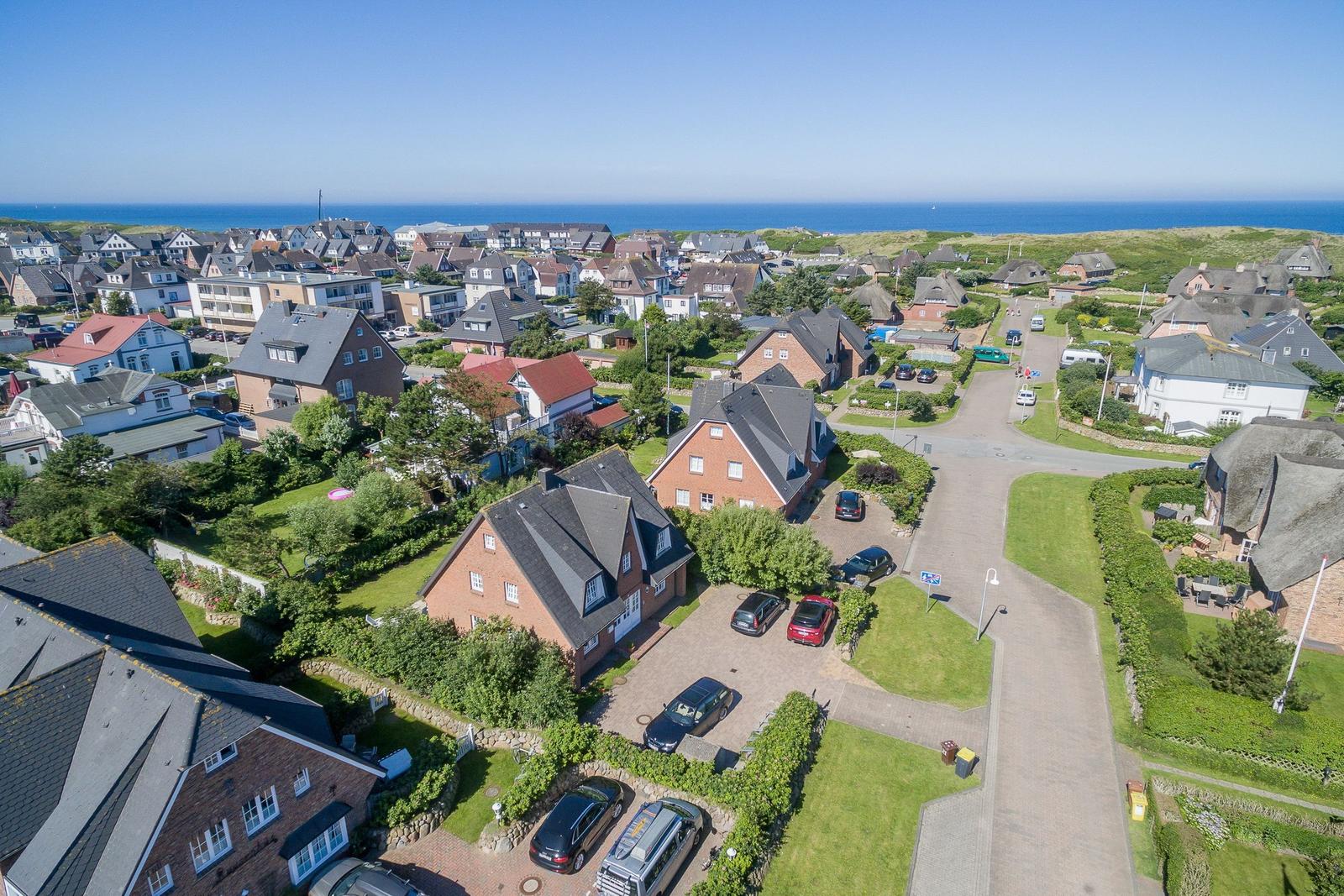 Aerial view of a coastal village with houses, gardens, and the sea in the background.