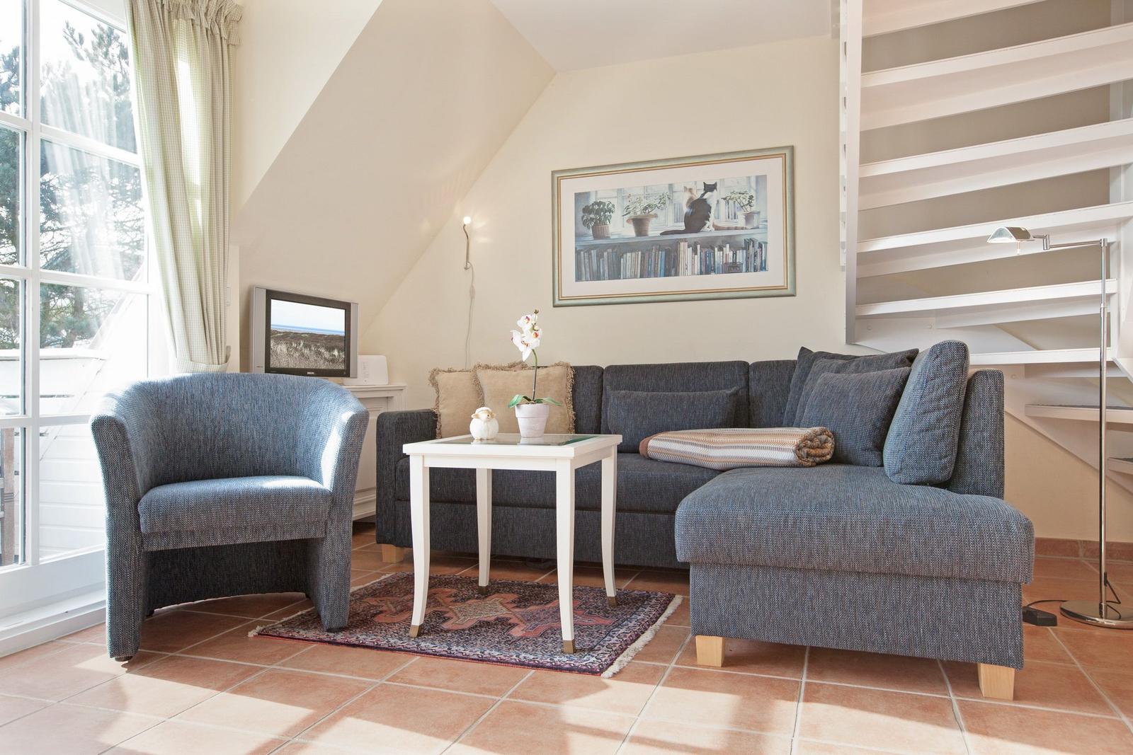 Living room with sofa, armchair, table, and wall art. Patio door and staircase visible.