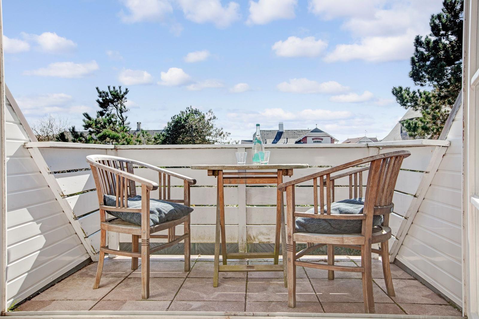 Terrace with table and two chairs, view of sky and trees.