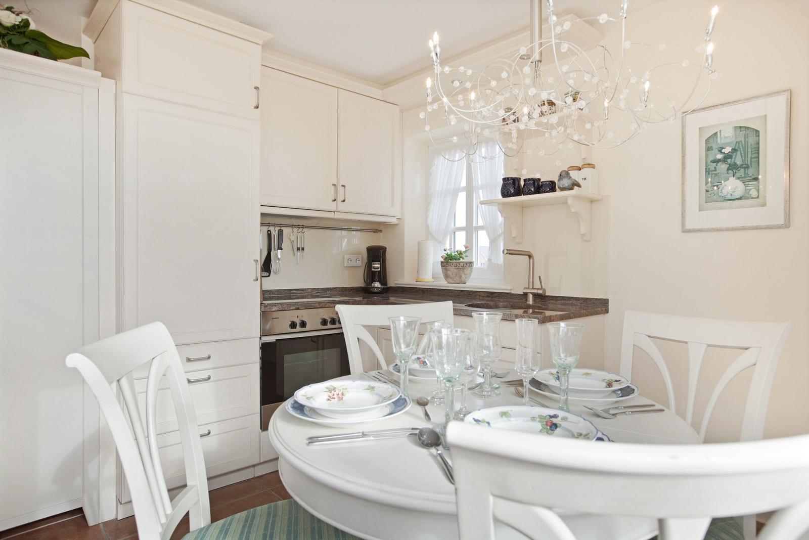 Dining area with white table and chairs, kitchenette, and chandelier.