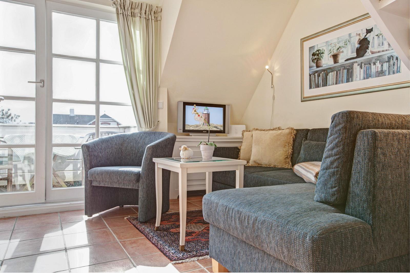 Living room with sofa, armchair, and TV. Windows with balcony view.