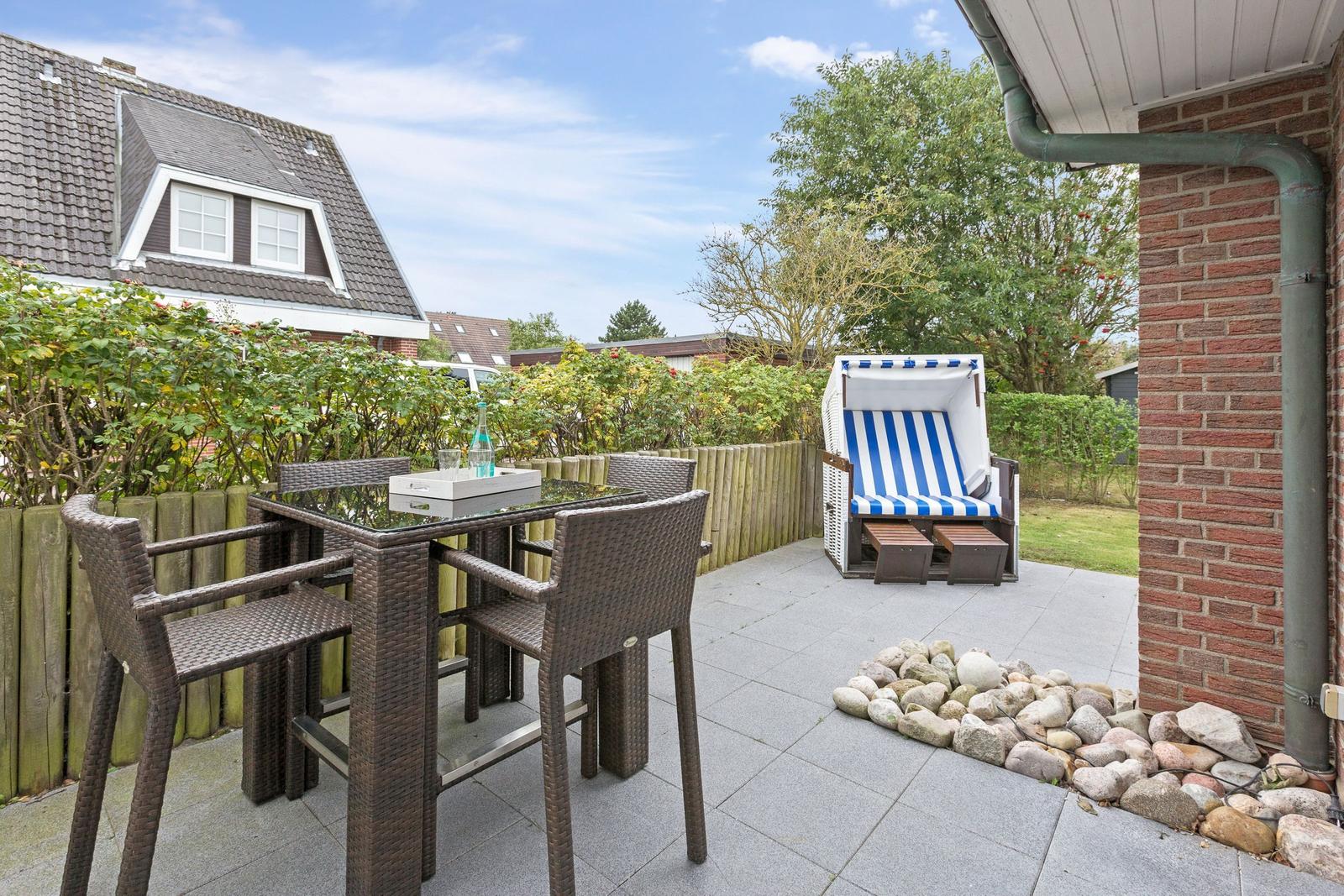 Terrasse mit Tisch, Stühlen und Strandkorb. Hinterhof mit Hecke und Steinbeete.