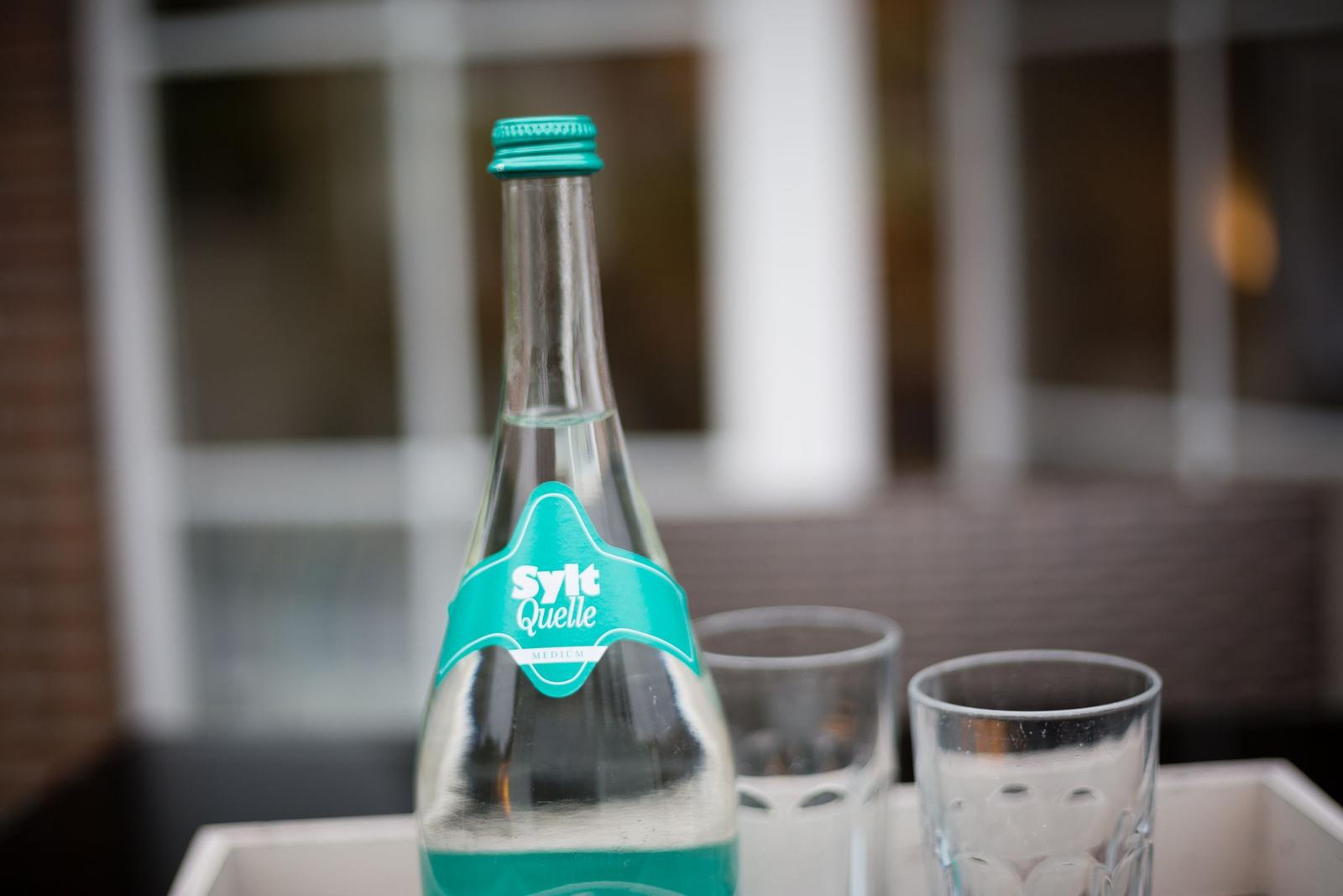 Eine Flasche Sylt Quelle Mineralwasser mit zwei Gläsern auf einem Tisch.