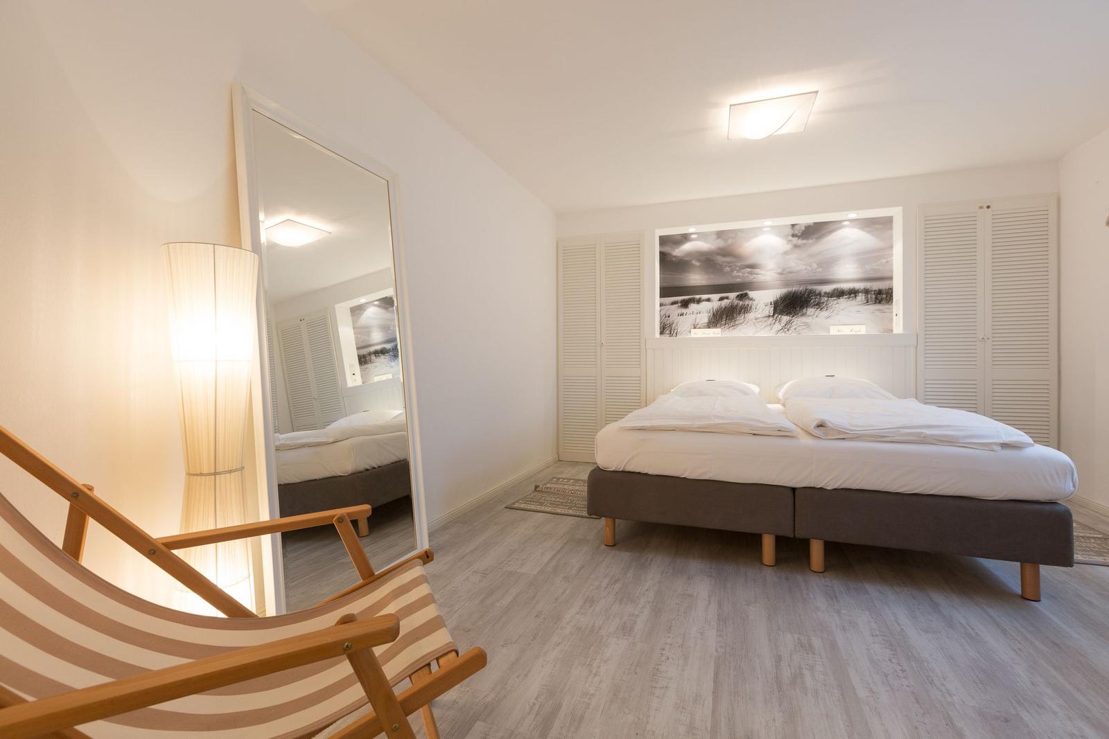 Schlafzimmer mit Bett, Spiegel und Stehlampe. Wandbild und Holzboden.