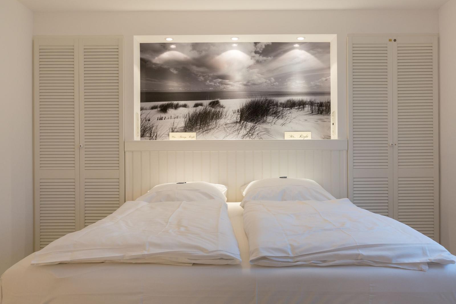 Doppelbett mit weißen Laken unter einem Wandbild mit Strandmotiv.