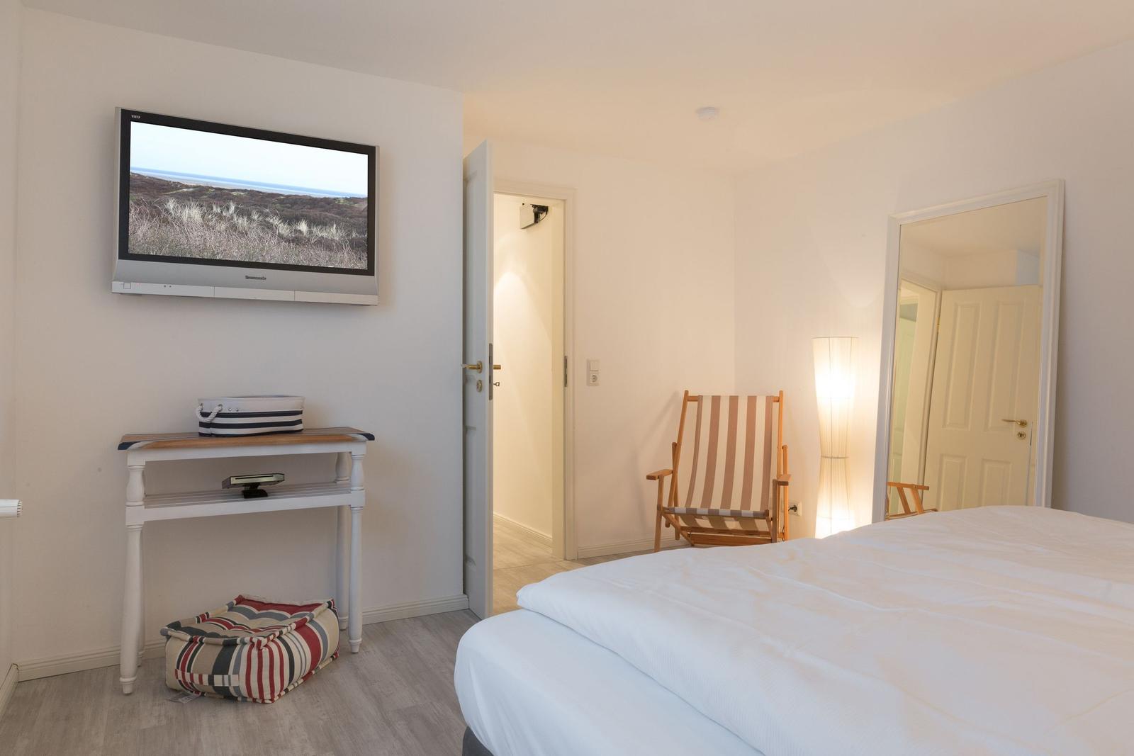 Schlafzimmer mit Bett, Fernseher und Stuhl.