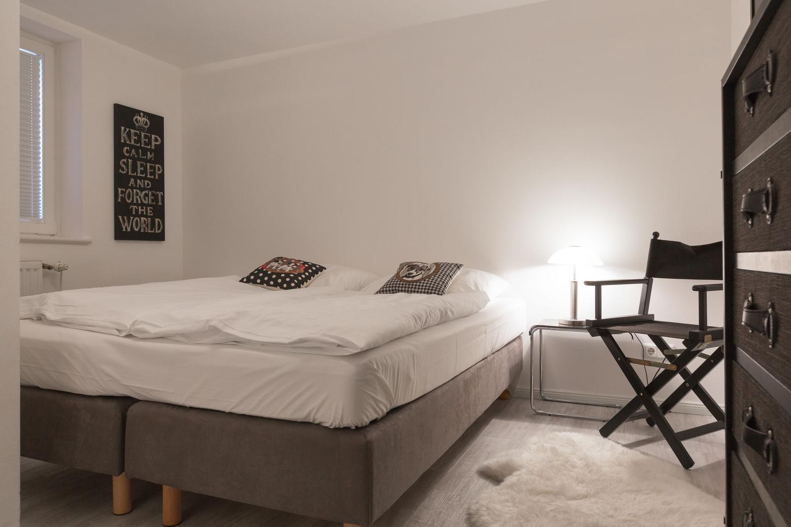 Schlafzimmer mit Bett, Nachttisch, Stuhl und Wandbild.