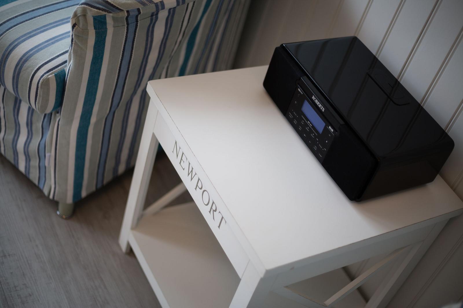 Schwarzener Radio auf weißem Tisch neben gestreiftem Sofa.