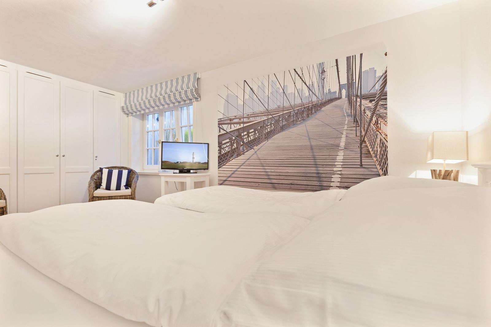 Schlafzimmer mit großem Bett, Wandbild einer Brücke und Fenster mit Vorhang.