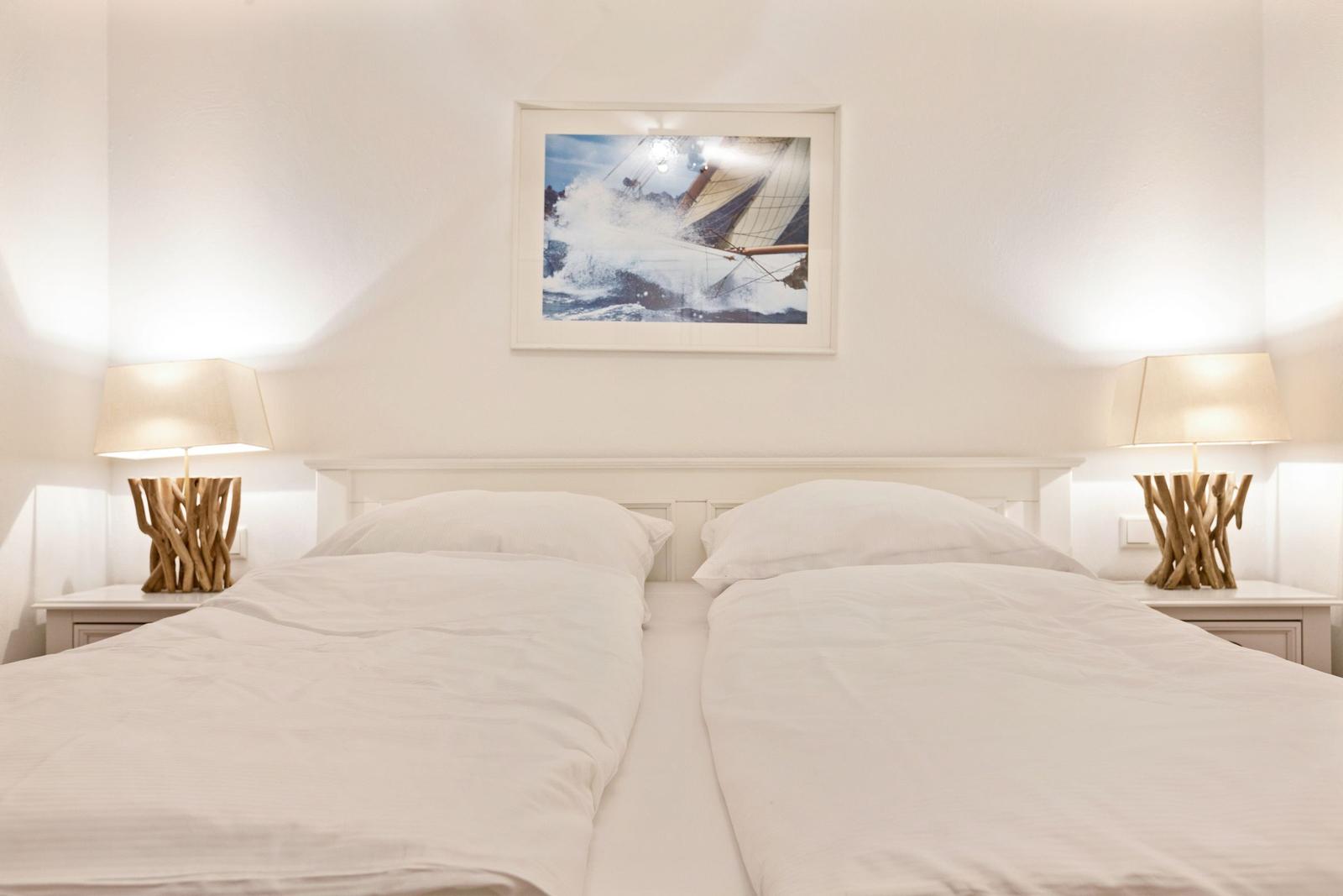 Zwei Betten mit weißen Bettwäschen, zwei Nachttische mit Lampen und ein Bild an der Wand.