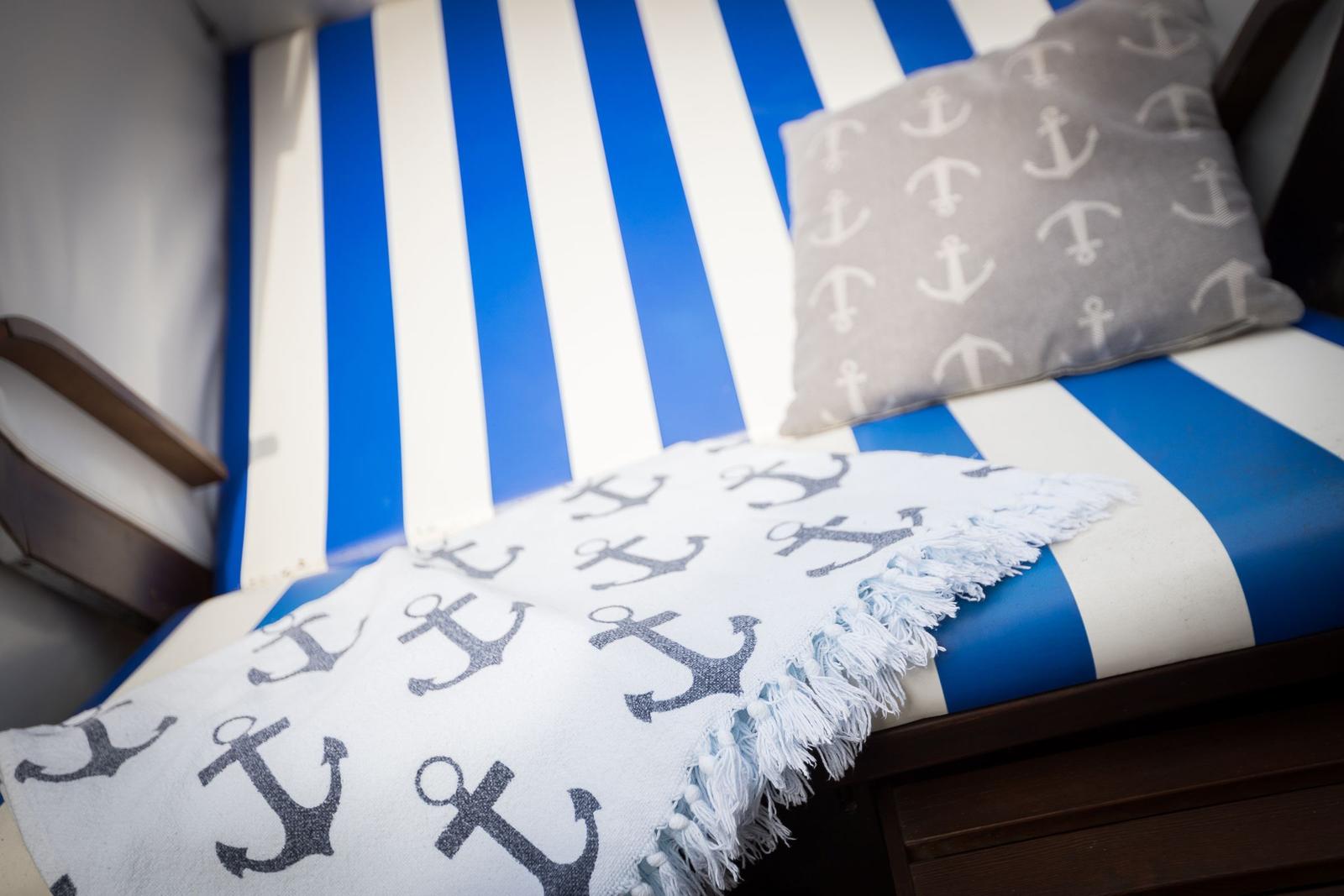 Sofa mit blau-weiß gestreiftem Bezug und Anker-Motiv-Kissen und Decke.