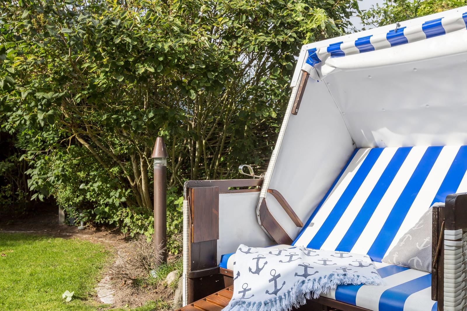 Strandkorb mit blau-weißem Streifenmuster und Ankermotivdecke im Garten.