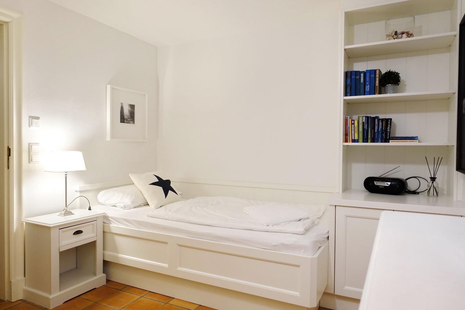 Ein Schlafzimmer mit weißem Bett, Nachttisch und Bücherregal.