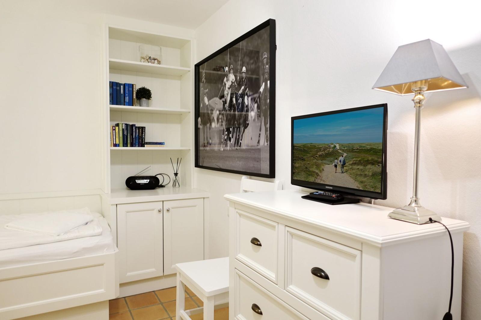 Schlafzimmer mit weißem Schrank, Fernseher und Wandbild.