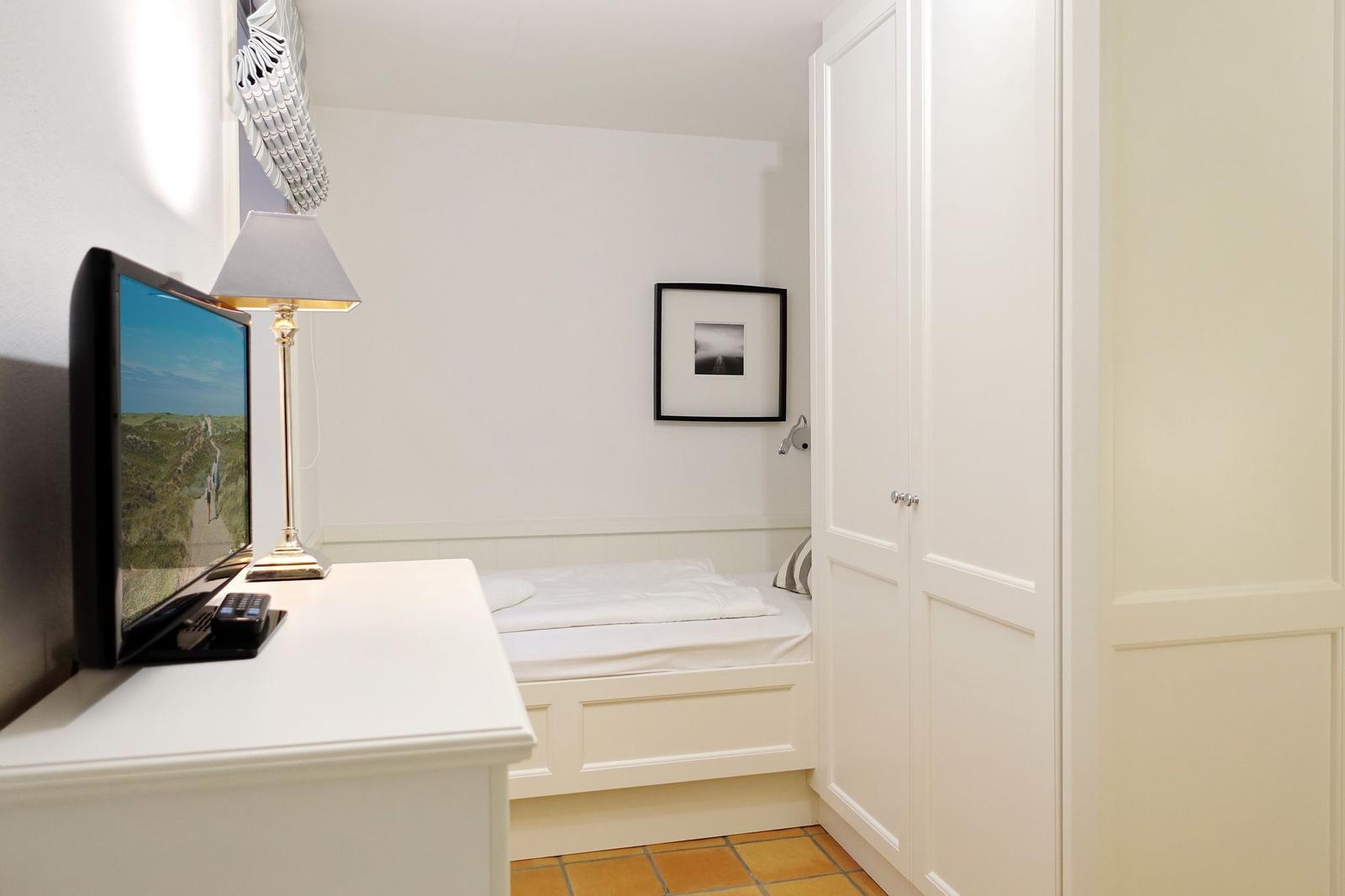 Schlafzimmer mit Bett, Schrank und TV-Tisch. Wandbild und Lampe sichtbar.