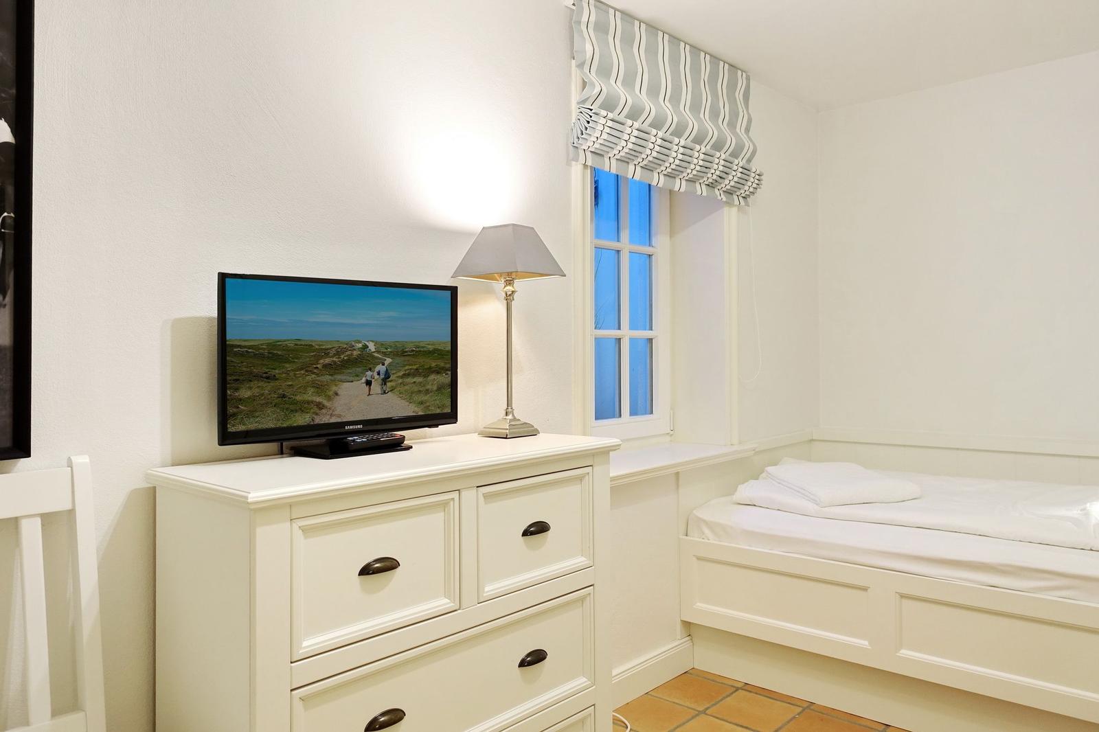 Schlafzimmer mit Bett, Schrank und Fernseher an der Wand.