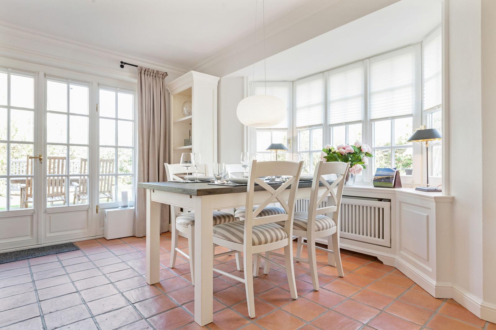 Esszimmer mit Tisch, Stühlen und Fenstern. Terrasse über Glastüren.