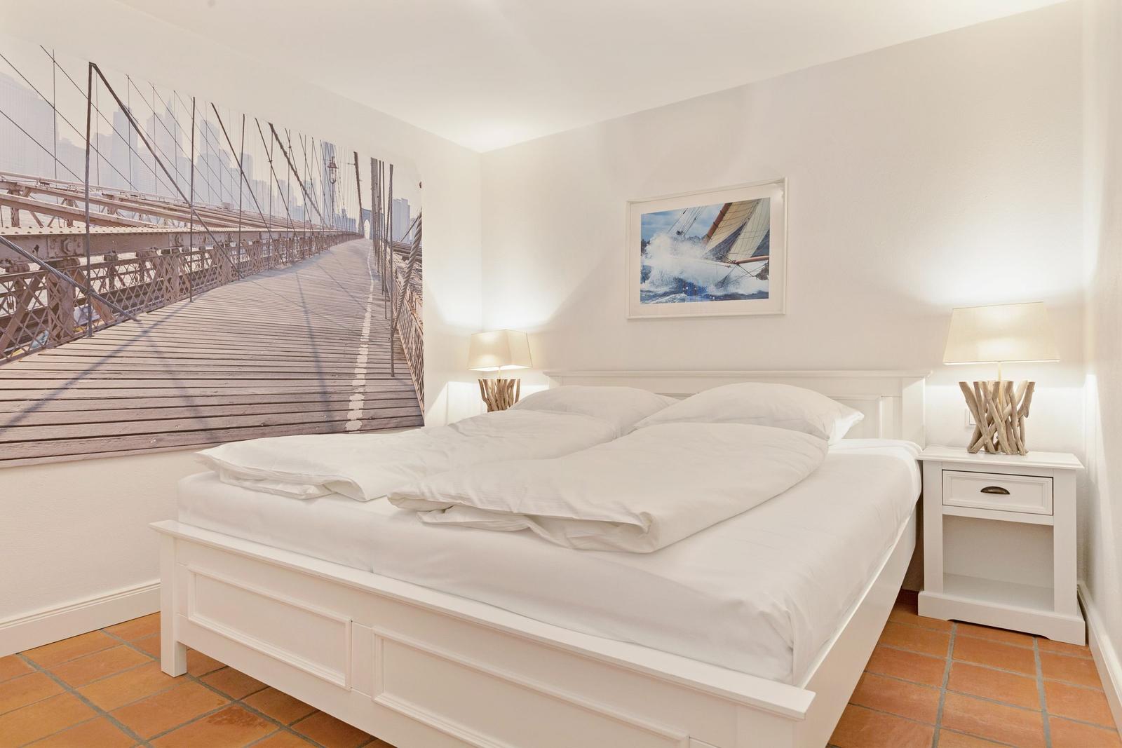 Schlafzimmer mit weißem Bett, Wandbild einer Brücke und zwei Nachttischen mit Lampen.