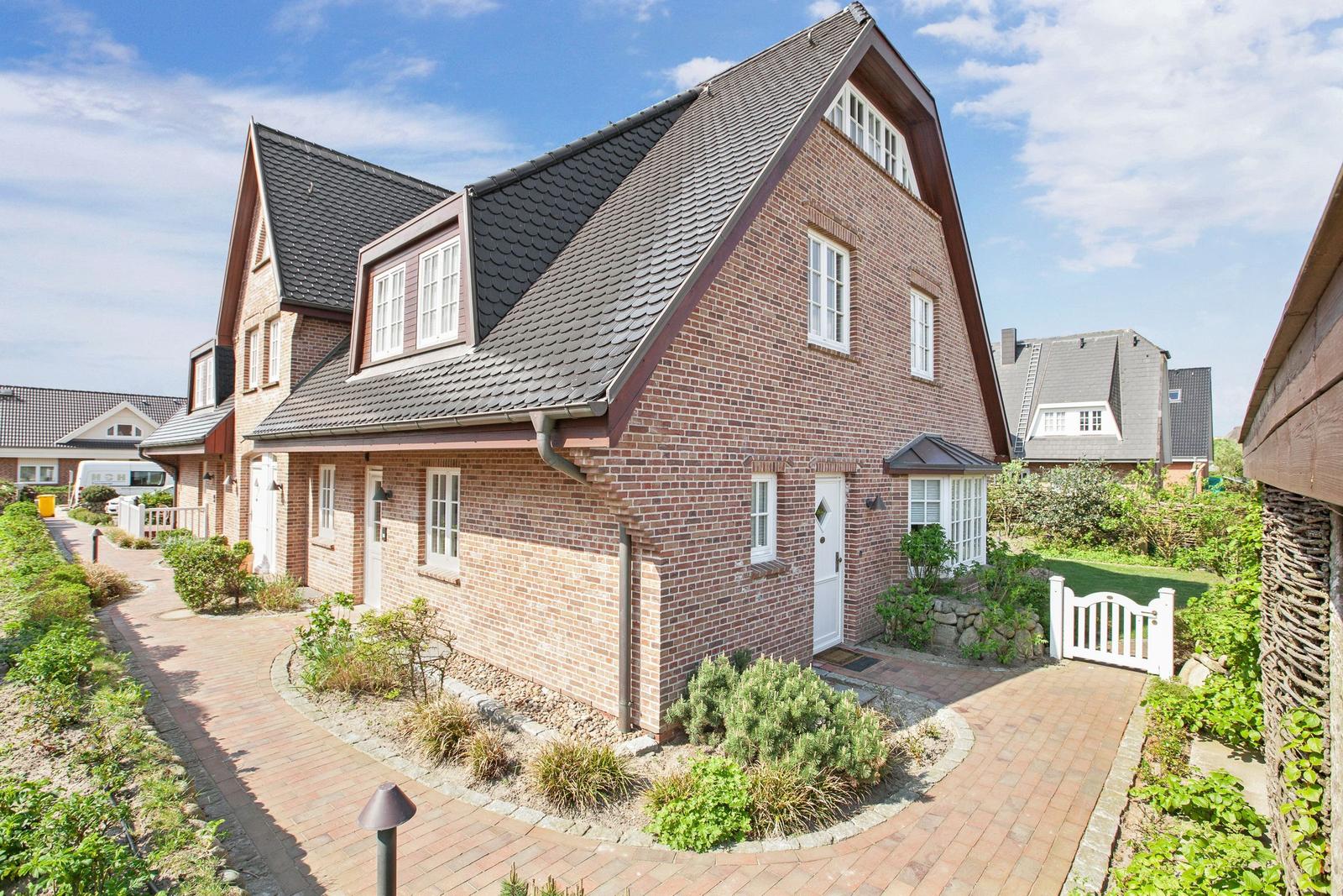 Ein zweistöckiges Haus mit rotem Backstein, dunklem Dach und weißer Tür.