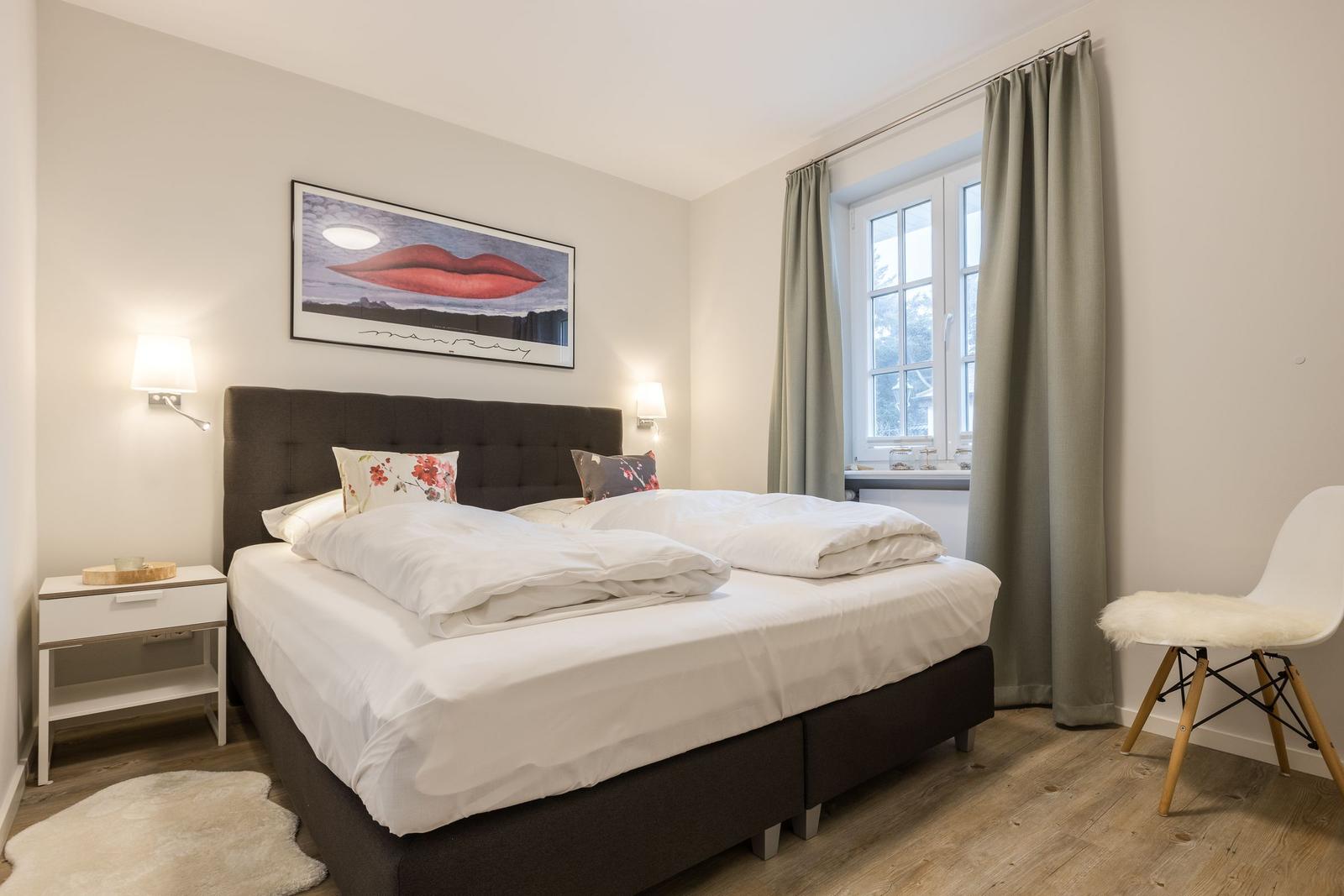 Schlafzimmer mit Doppelbett, Fenster, Vorhang und Stuhl.