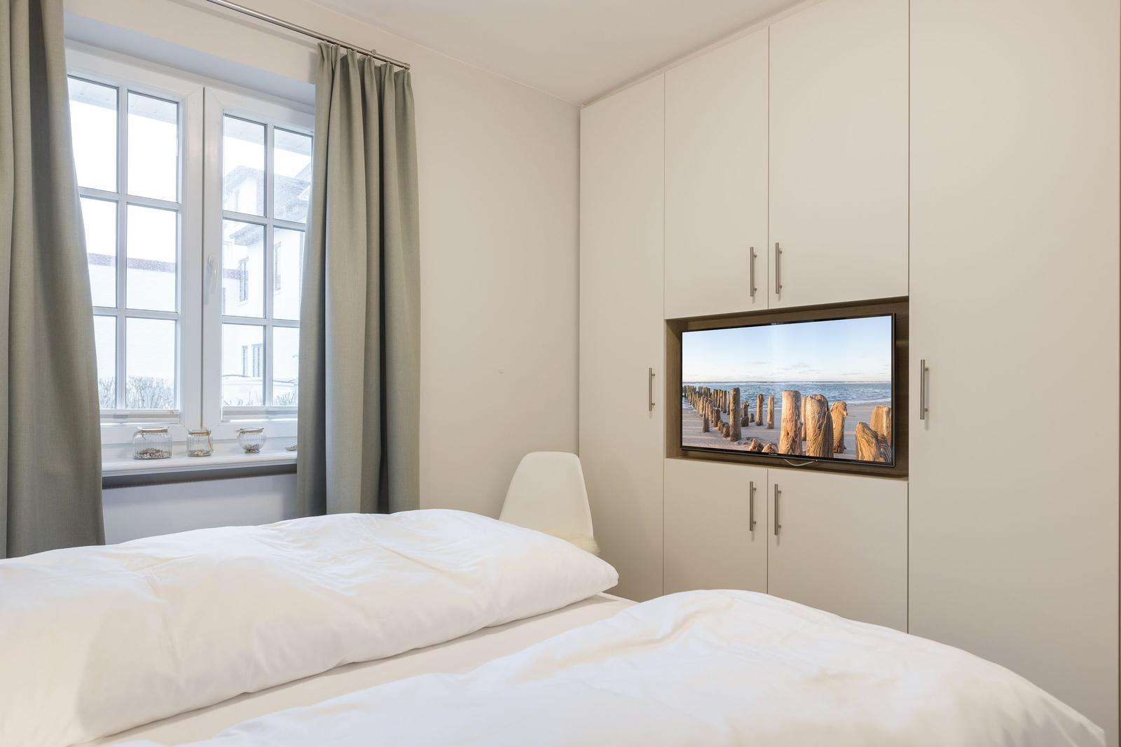 Schlafzimmer mit Bett, Fenster und eingebauter TV-Anlage.