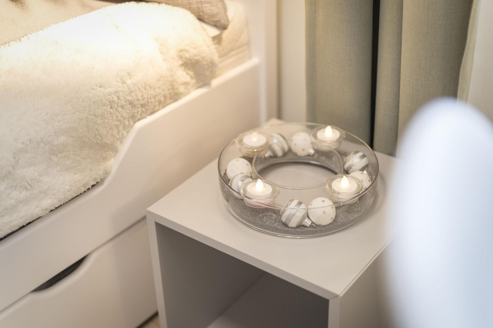 Schlafzimmer mit Nachttisch und Kerzenkranz. Bett mit Felldecke.