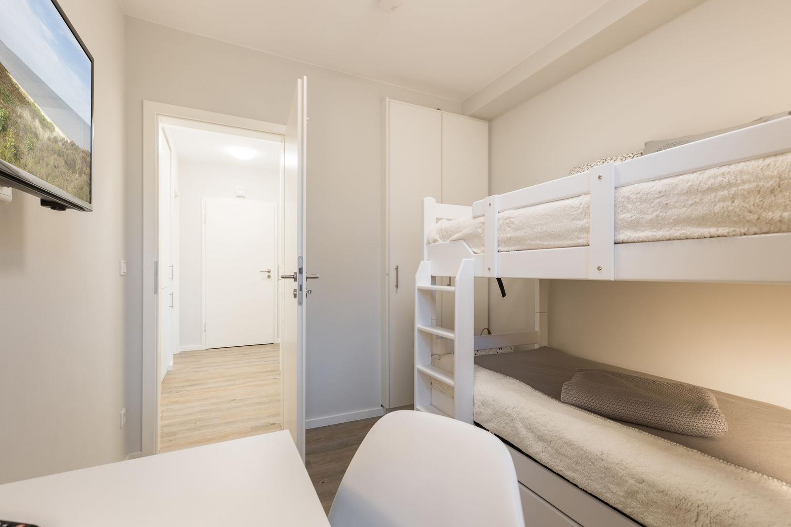 Zimmer mit Doppelstockbett, Schrank und Fernseher an der Wand.