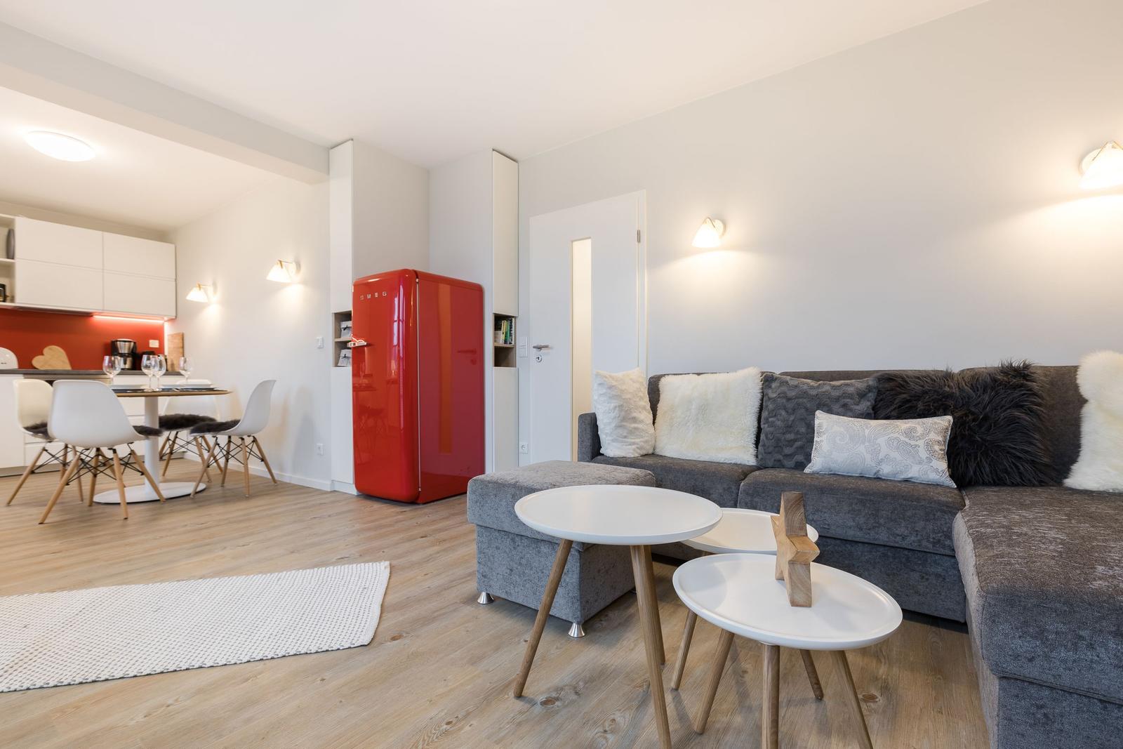 Wohn- und Essbereich mit grauem Sofa, rotem Kühlschrank und Holzboden.