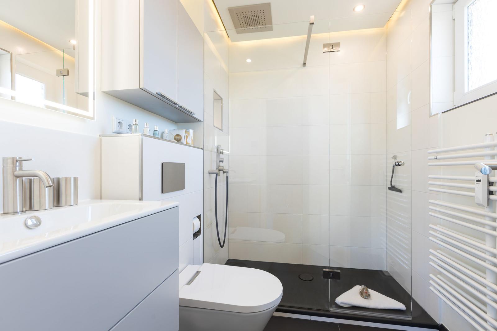 Modern shower with glass enclosure, sink, and toilet in white color scheme.