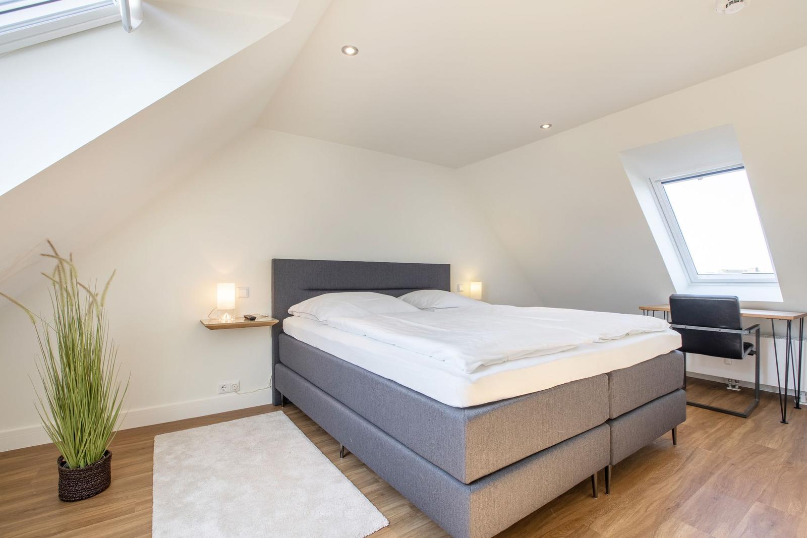 Bedroom with sloped ceilings, bed, desk, and plant.