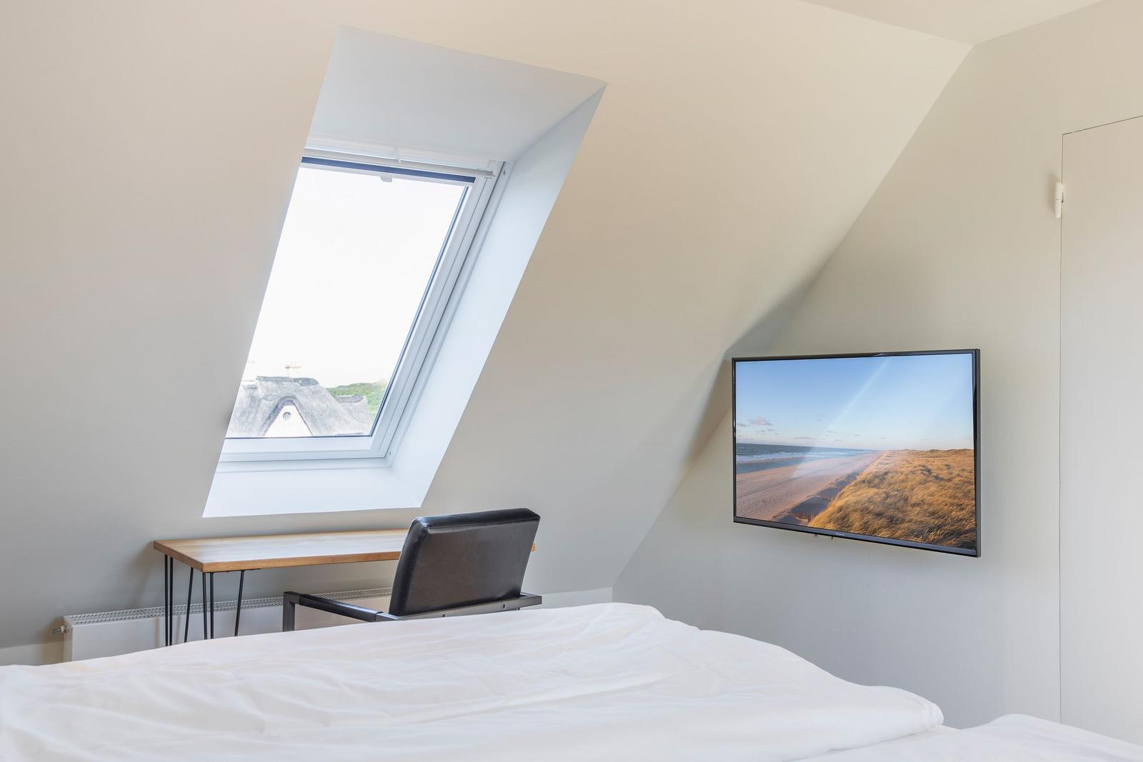 Bedroom with skylight, desk, and wall-mounted TV.