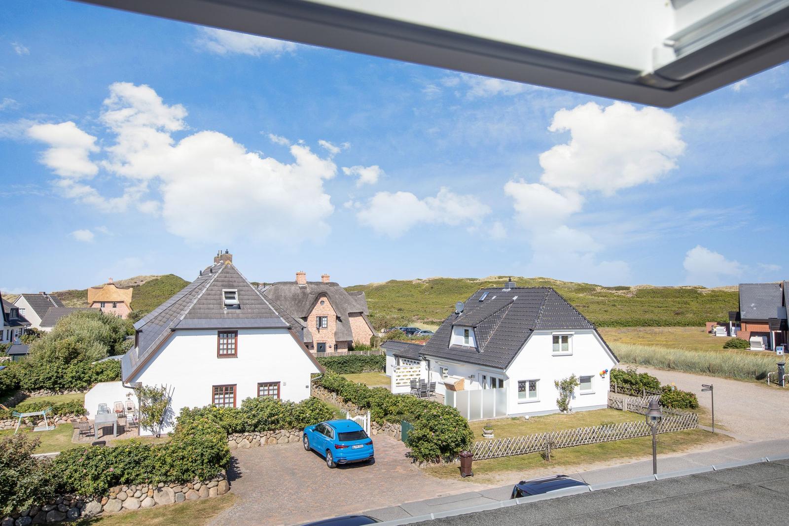 Wide view of houses with roofs and green slopes under blue sky.