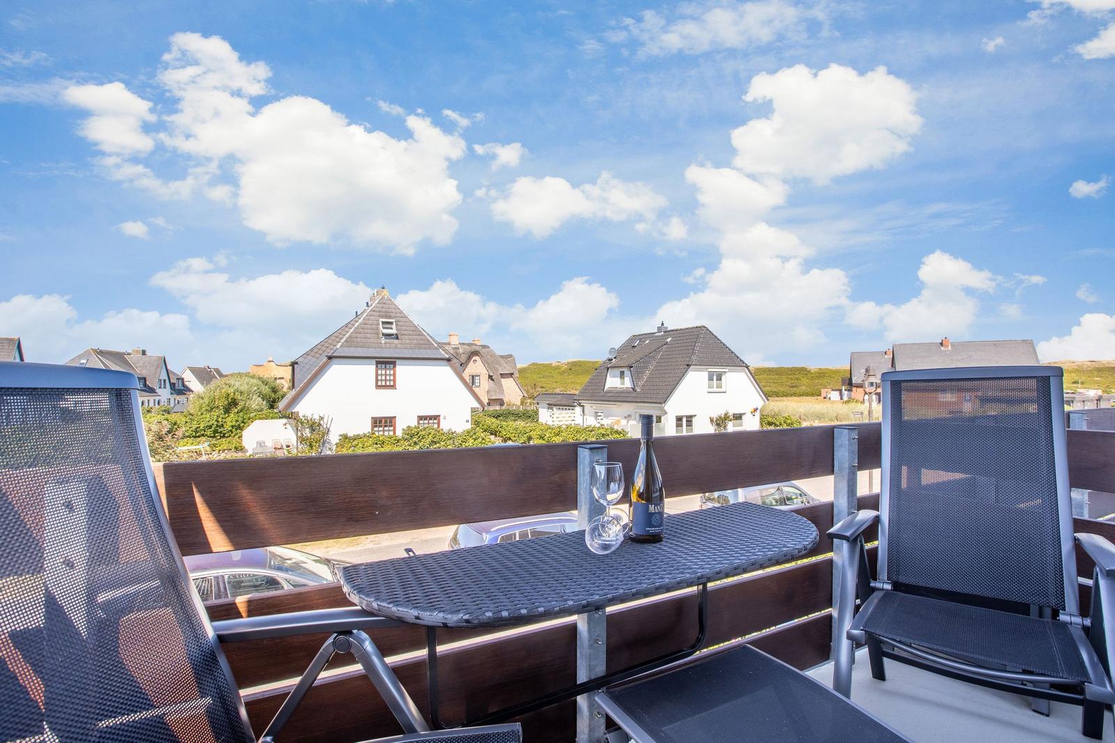 Terrace with table, two chairs, and wine bottle. View of houses and sky.