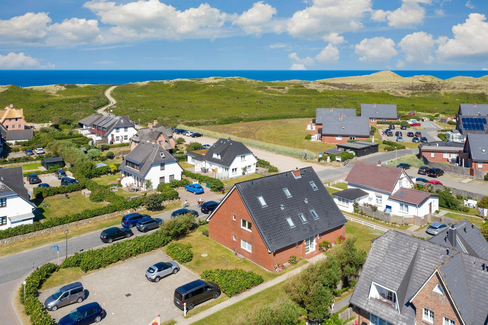 House with dormers and garden, surrounded by other houses and green areas. Sea in the background.