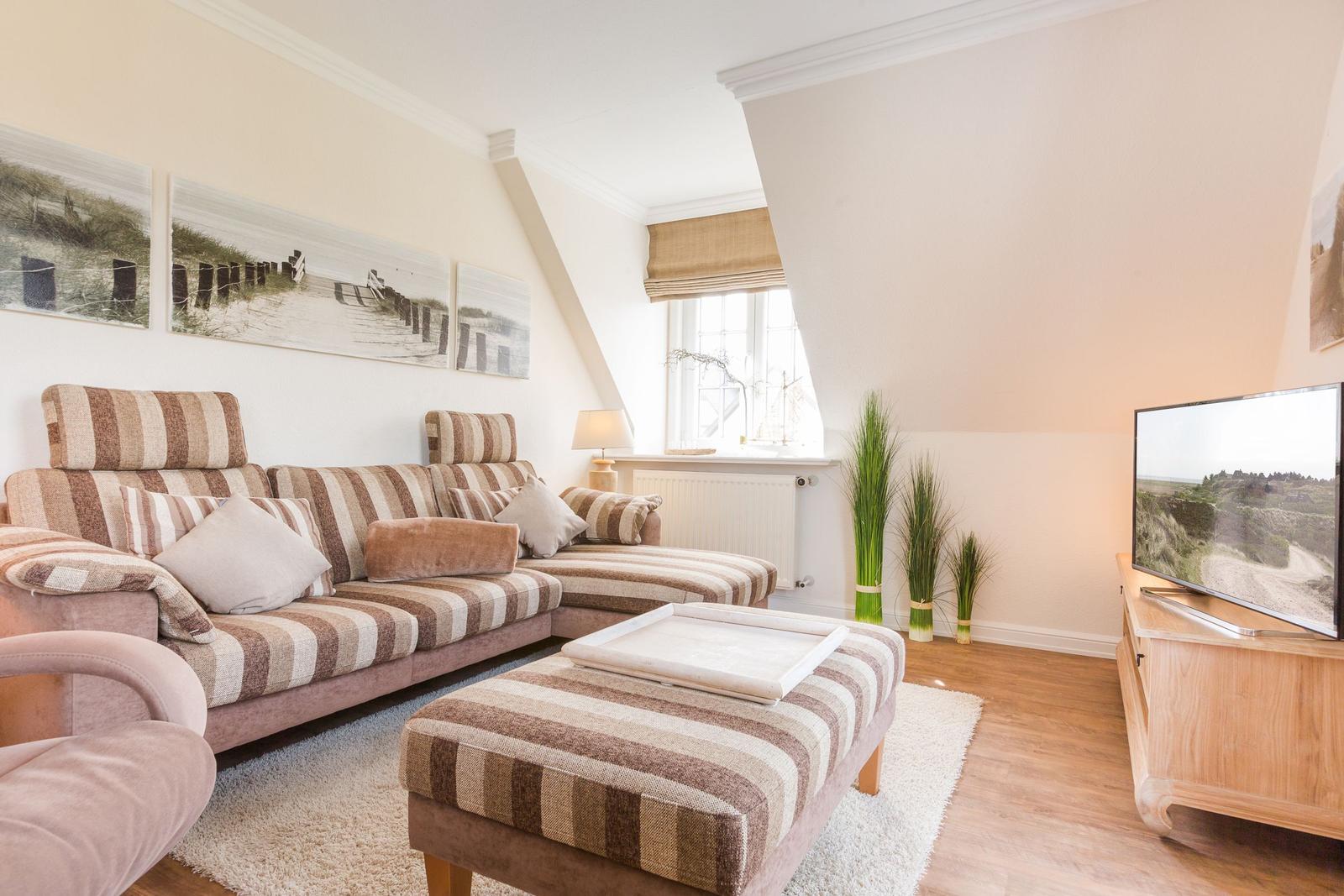 Wohnzimmer mit Sofa, Couchtisch und Fernseher. Wandbilder und Pflanzen sorgen für eine gemütliche Atmosphäre.