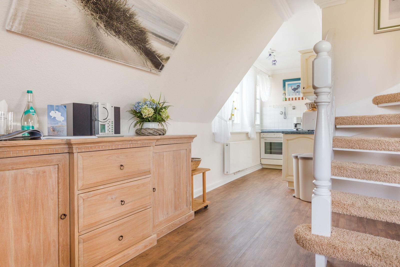 Eingangsbereich mit Holzschrank, Treppe und Blick in die Küche.