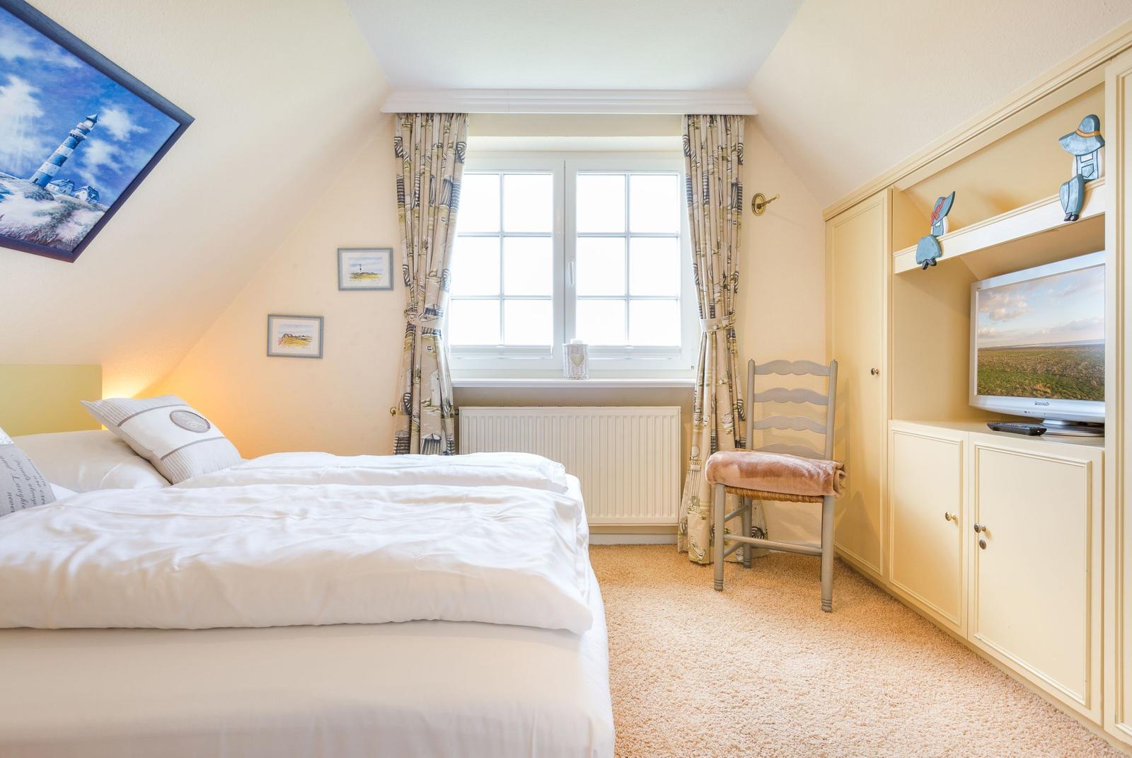 Schlafzimmer mit Doppelbett, Fenster, Stuhl und TV-Einbau