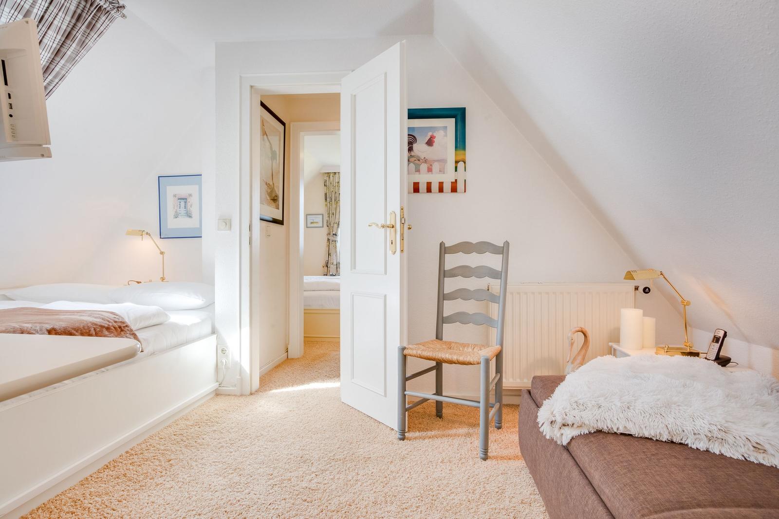 Schlafzimmer mit zwei Betten, Stuhl und Tür zum Anschlussraum.