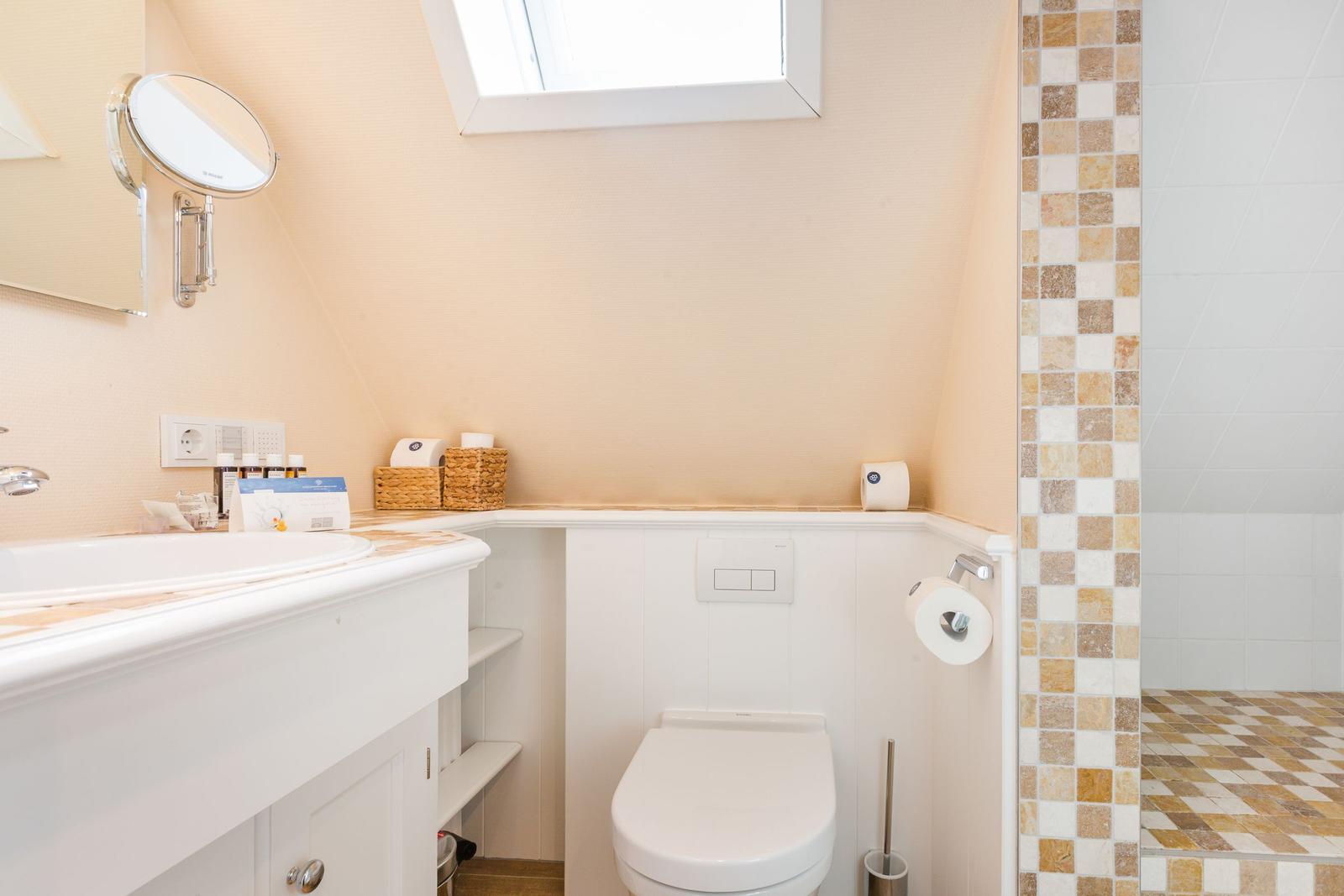 Badezimmer mit Waschbecken, Toilette und Dusche. Dachfenster und Mosaikfliesen.