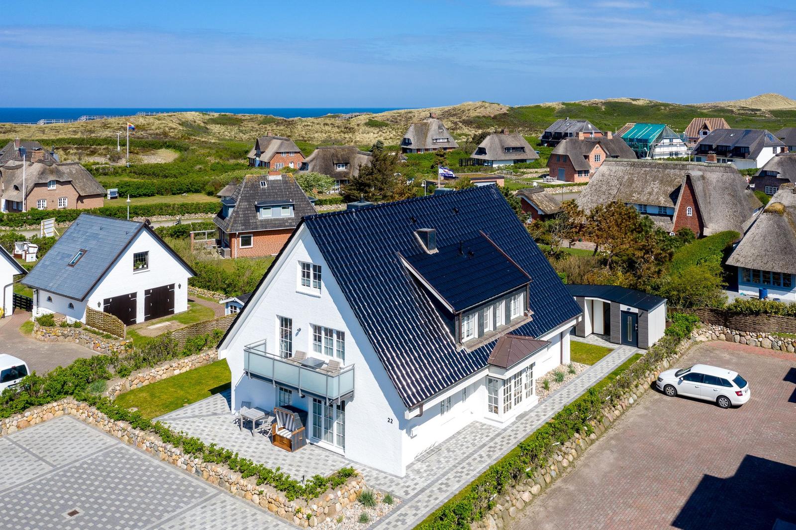 Moderne weiße Villa mit Balkon und Terrasse. Hintergrund: Strand und Dünen.