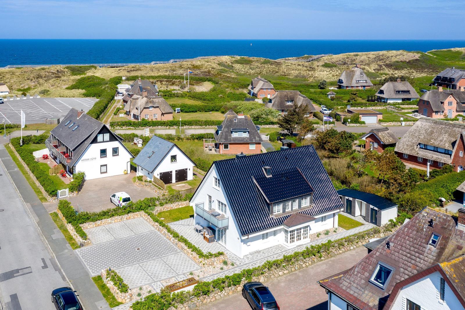Haus mit dunklem Dach, umgeben von Grünflächen und dem Meer.