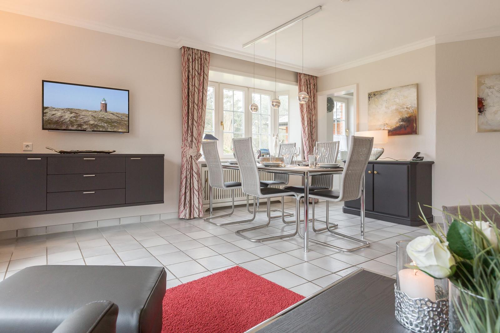 Living and dining area with TV, table and chairs, windows and curtains.