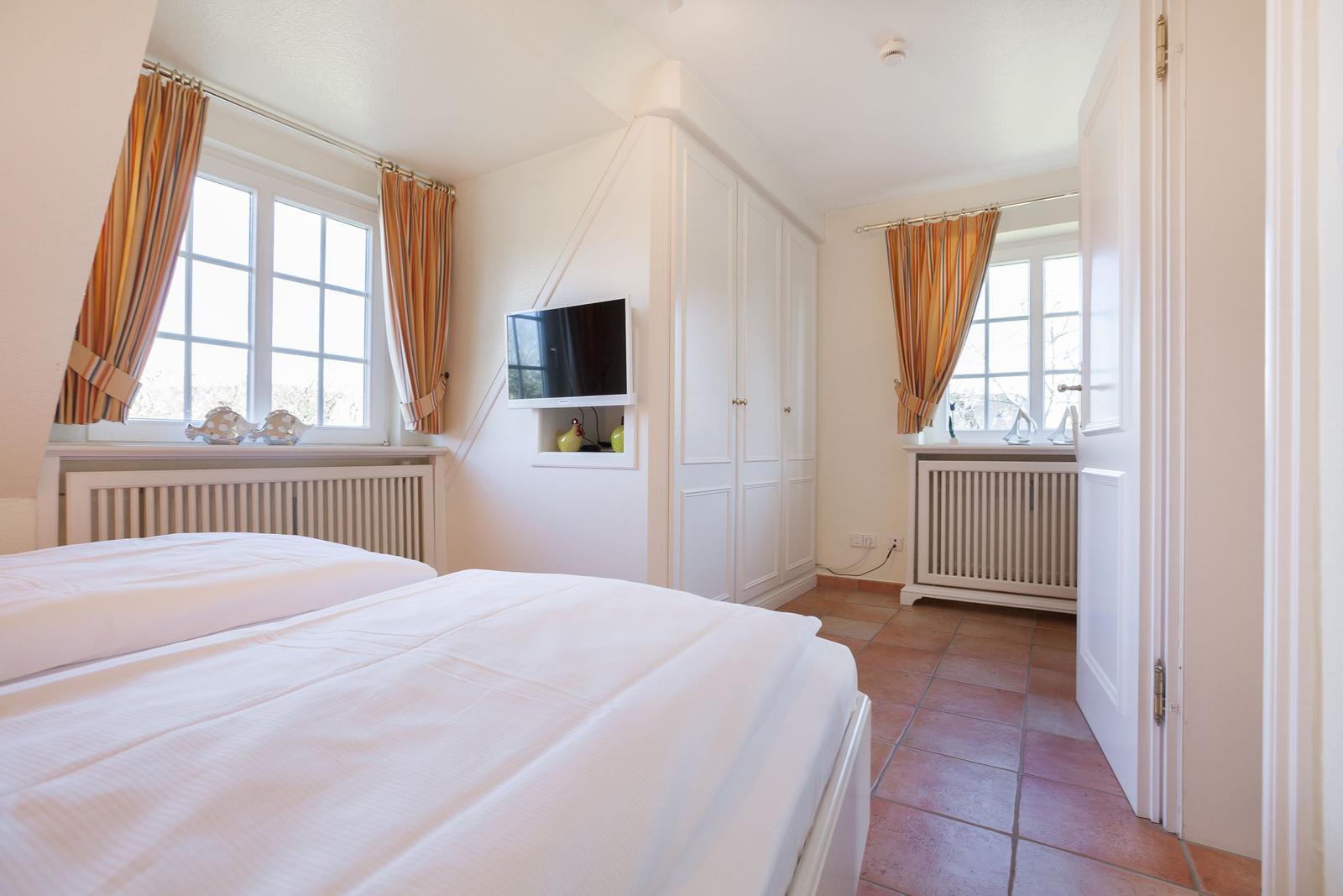 Room with double bed, TV, and two windows with curtains.