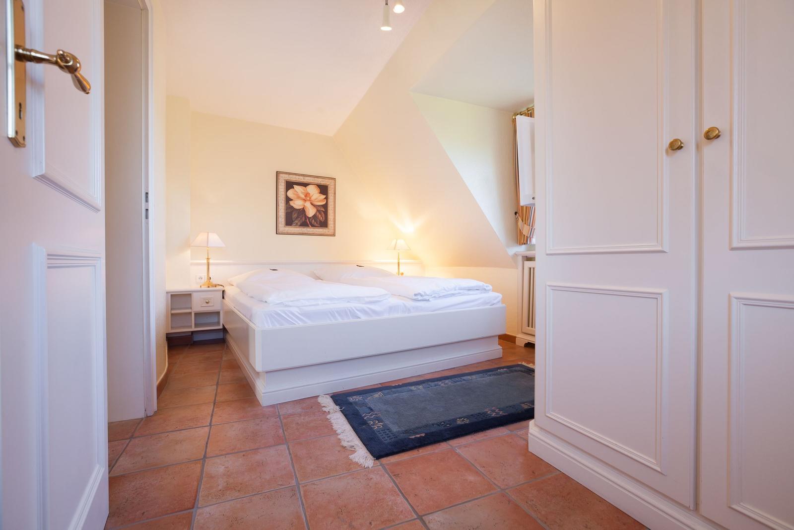 Bedroom with sloped ceiling, white bed, and tiled floor