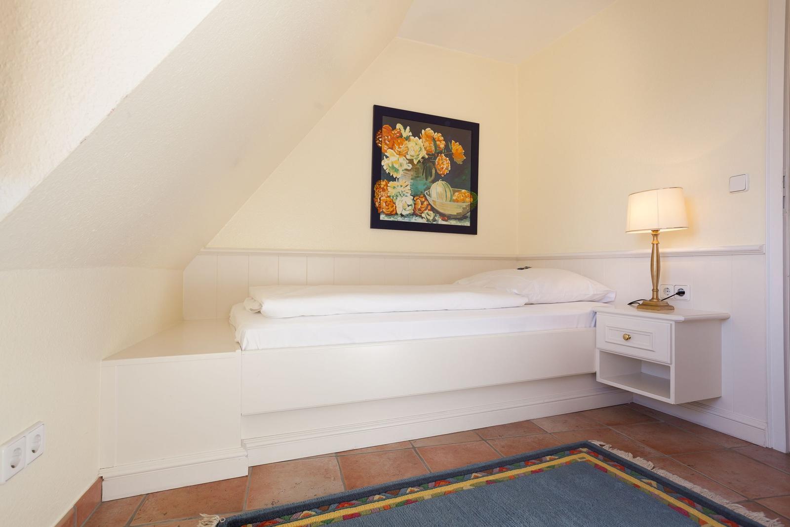 Bedroom with sloped ceiling, bed, nightstand, and wall art.