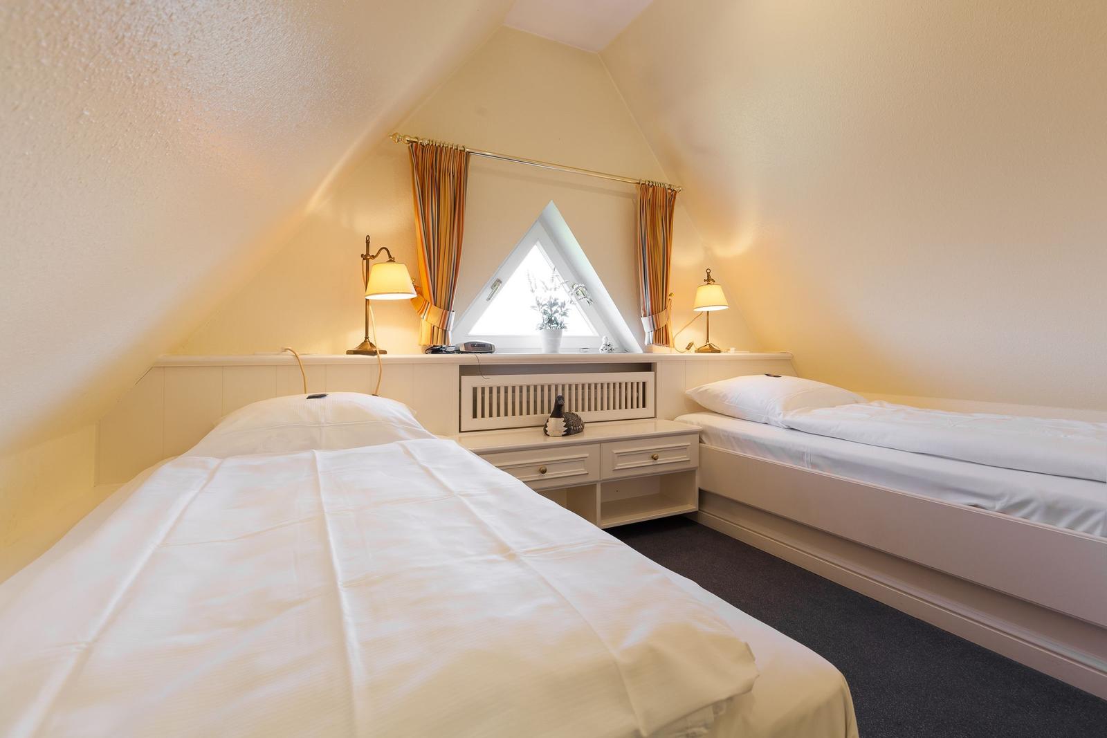 Two beds under sloped ceiling with window and nightstand.
