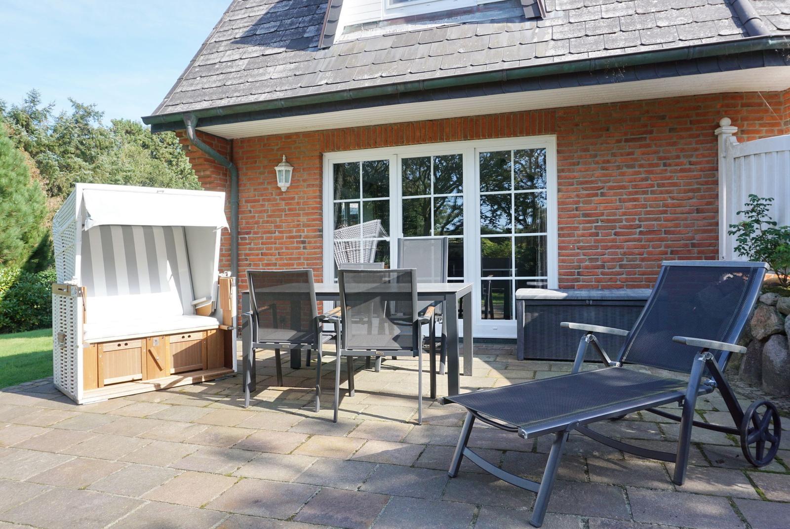 Terrace with lounge chair, table, chairs, and beach cabana in front of red brick house.