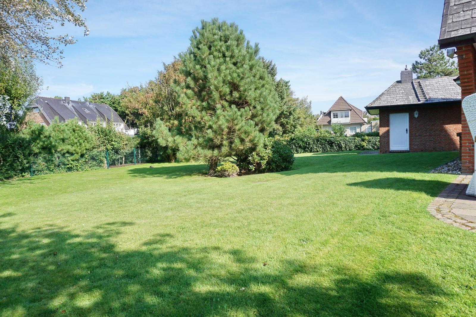 Large green garden with tree and house in background.